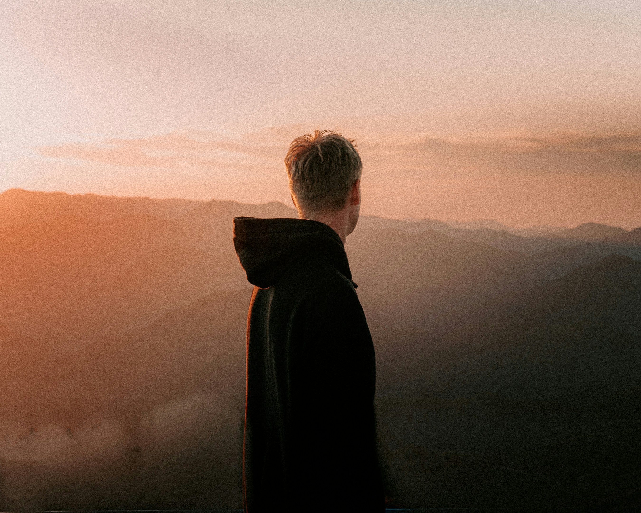 Joven contemplando el horizonte montañoso al atardecer, simbolizando visión y propósito